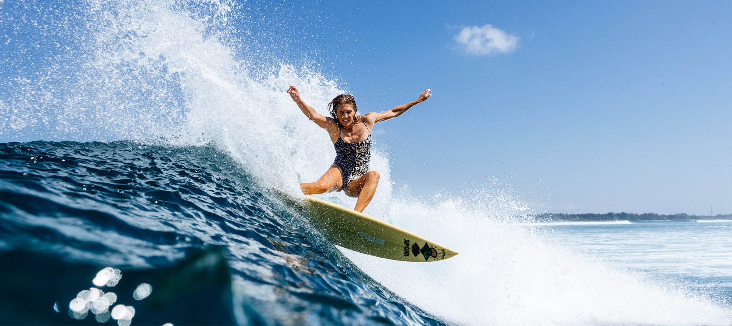 Stephanie Gilmore surfing on a wave with a clear blue sky
