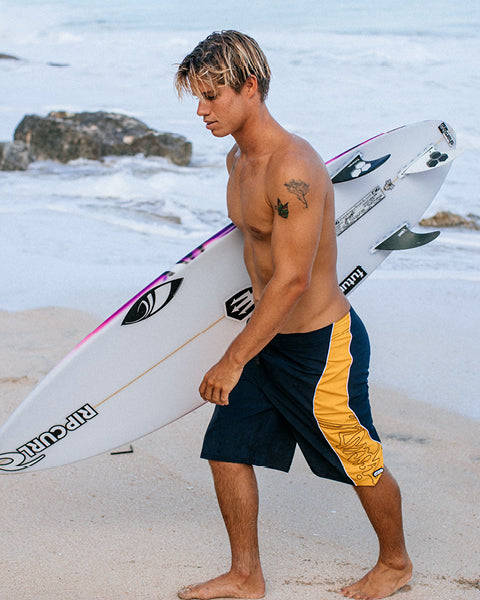 Man holding a surfboard on a beach with ocean waves in the background