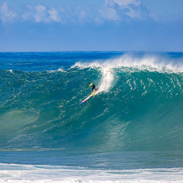 Surfer riding a large wave in the ocean with clear blue sky.