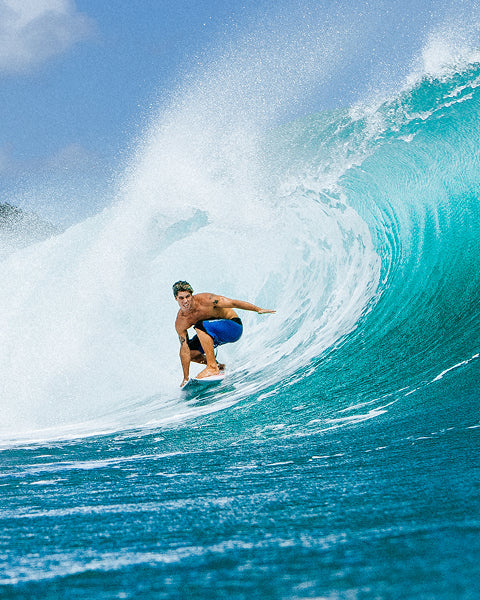 Surfer riding a large wave in the ocean with clear blue sky.