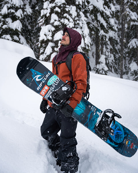 Person holding a snowboard in a snowy forest