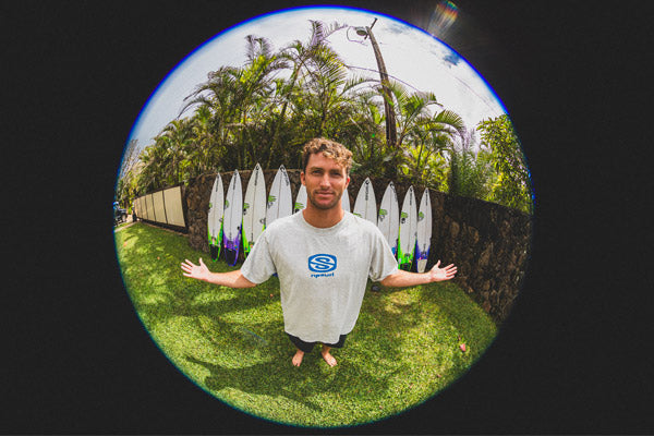 Crosby Colapinto with surfboards in the background, wearing a branded t-shirt.