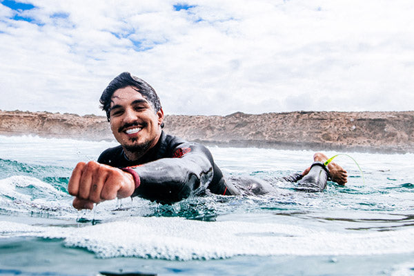 Gabriel Medina in a wetsuit paddling in the ocean with a scenic background
