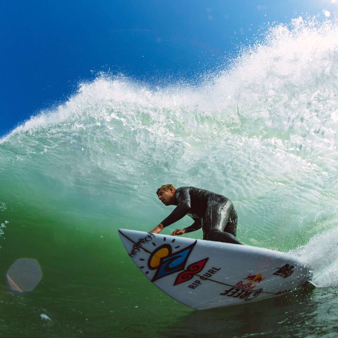 Surfer riding a wave on a colorful surfboard with a blue sky background