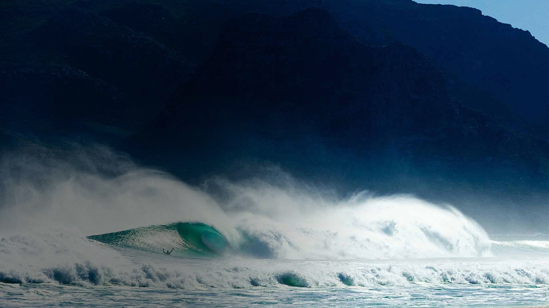 Surfer riding a large wave with a mountainous background