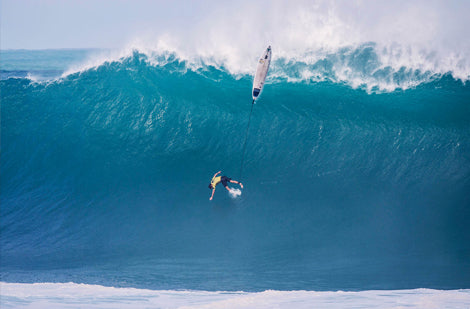 Surfer riding a large wave with a paddleboard in the air.