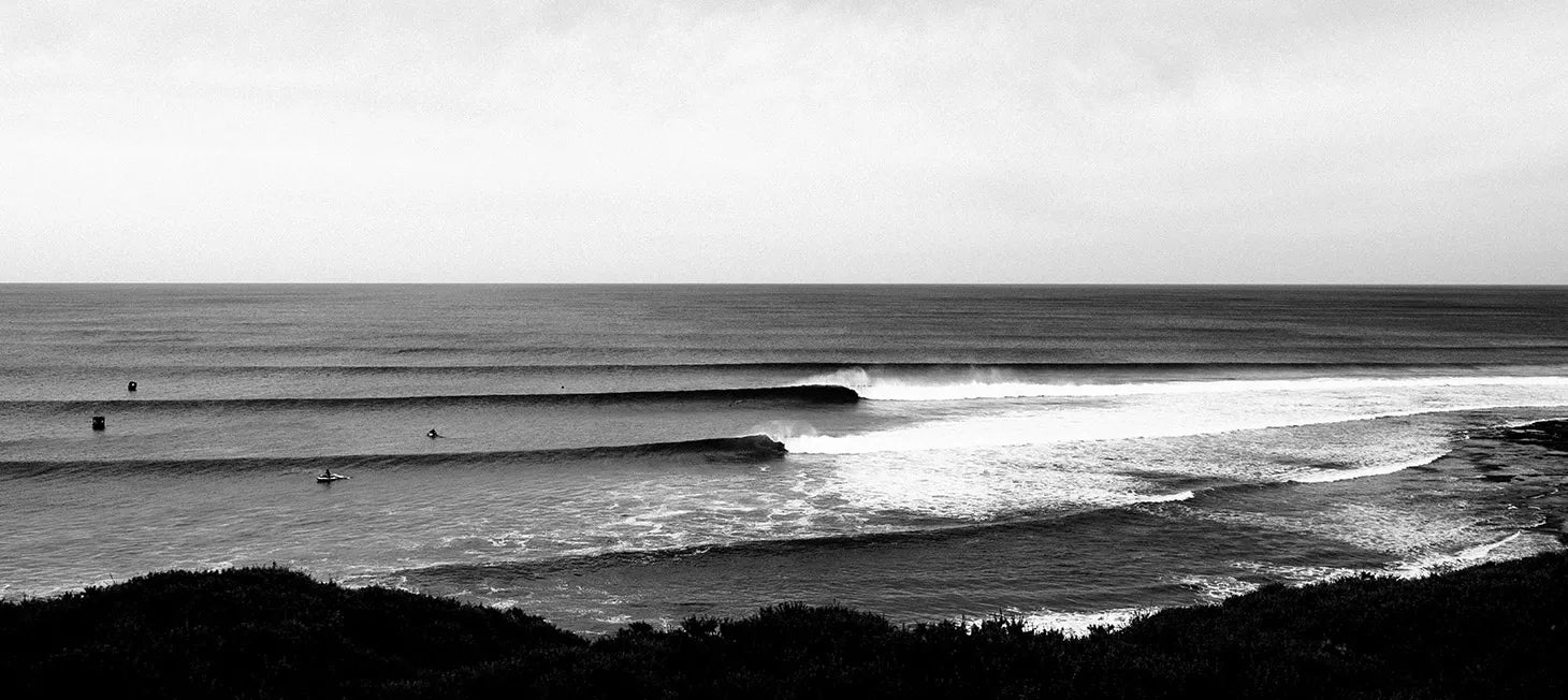 Black and white photo of a beach with waves and people in the water.