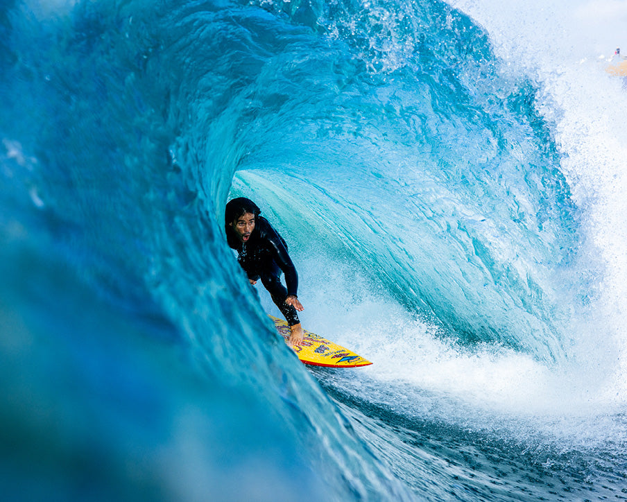 Person surfing inside a large blue wave on a yellow surfboard