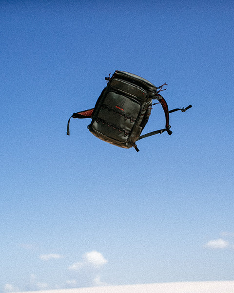 Black backpack floating in the air against a blue sky with white clouds