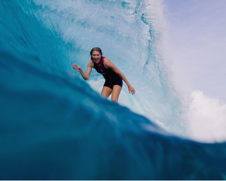 Person surfing a large wave with a clear sky in the background