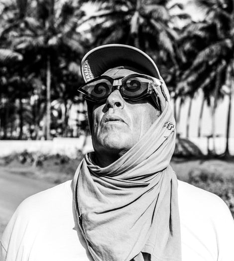 Tom Curren wearing sunglasses and a cap with palm trees in the background